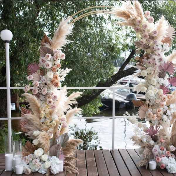 Tall floral arch with pastel roses and pampas grass beside white candles