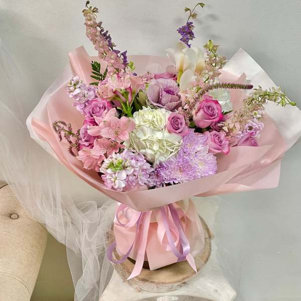Pink and lavender bouquet with roses, hydrangea, and lilies wrapped in pastel paper