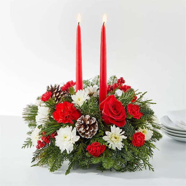 Red candles in a holiday floral centerpiece with white flowers and pinecones