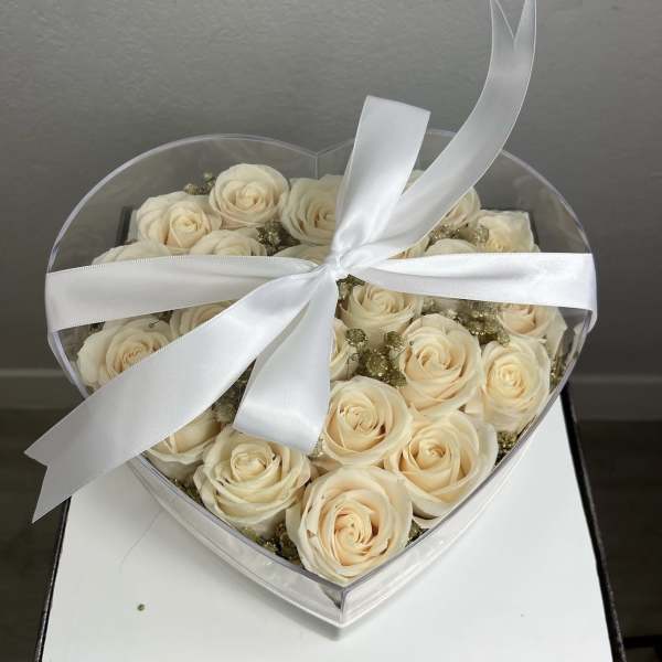 Cream roses in a clear heart-shaped box tied with a white ribbon