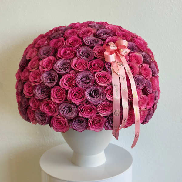 Round bouquet of pink and purple roses in a white vase with a pink ribbon