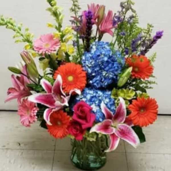 Colorful mixed bouquet in a glass vase with lilies, gerberas, roses, and hydrangeas