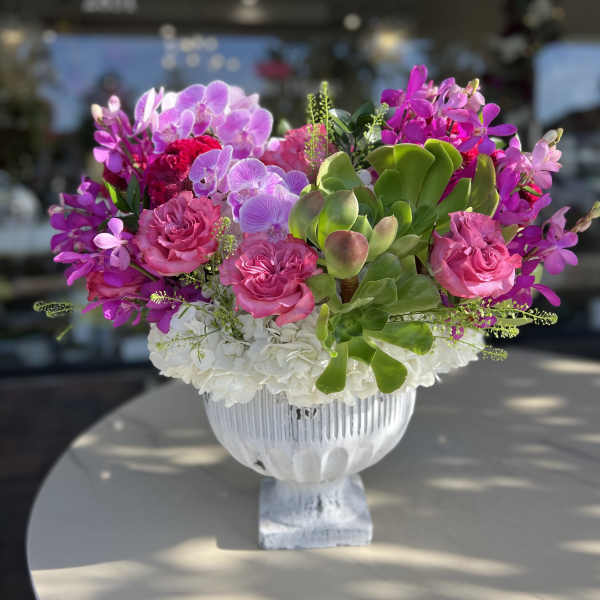Pink orchids and roses arranged in a white pedestal vase