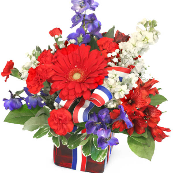 Red, white, and blue floral arrangement in a red glass vase with ribbon