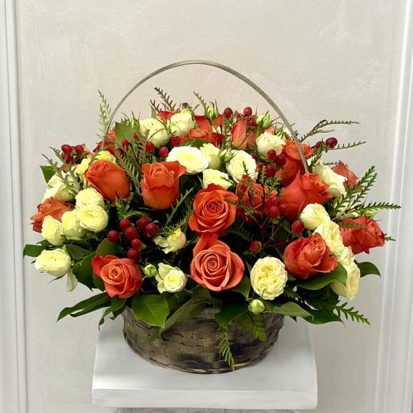 Basket arrangement of orange and white roses with red berries