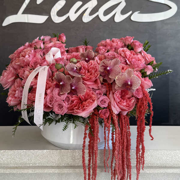Pink rose arrangement with orchids in a white bowl vase