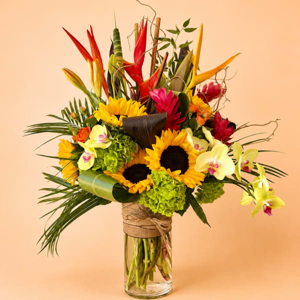 Tropical bouquet with sunflowers, orchids, and red heliconia in a glass vase