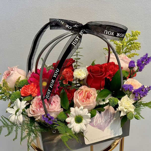 Mixed flower arrangement in a black handled basket with a ribbon bow