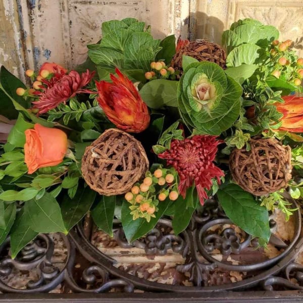 Low floral arrangement with orange roses and red blooms in a decorative container