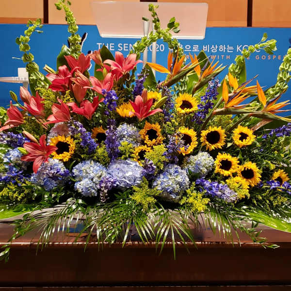 Large stage arrangement with yellow sunflowers, pink lilies, blue hydrangeas and orange tropical flowers.