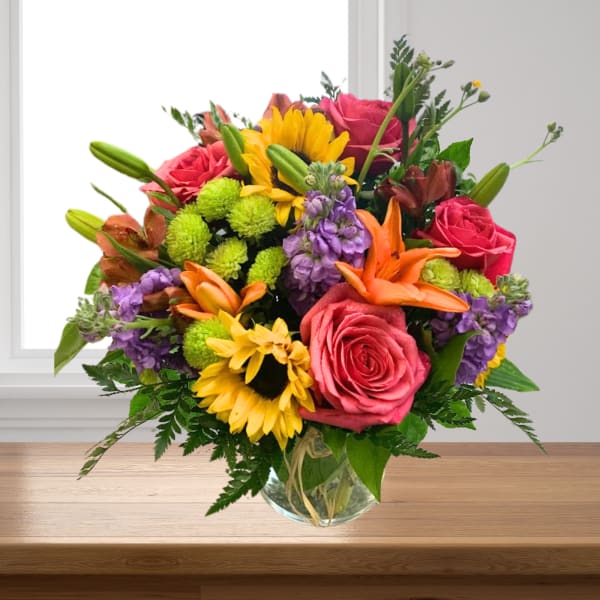 Mixed bouquet of roses, sunflowers, lilies, and purple flowers in a glass vase