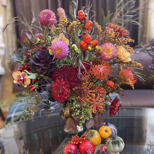 Colorful floral arrangement with pumpkins and grapes in a vase