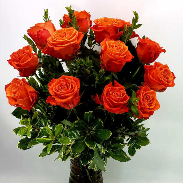 Orange roses arranged in a dark glass vase with variegated greenery