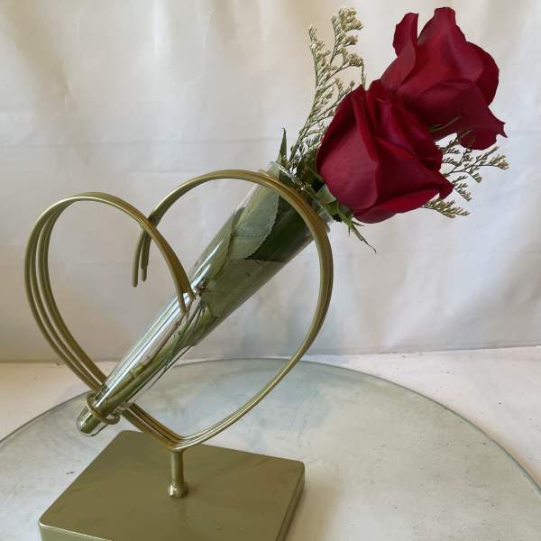 Two red roses in a clear cone vase on a gold heart stand