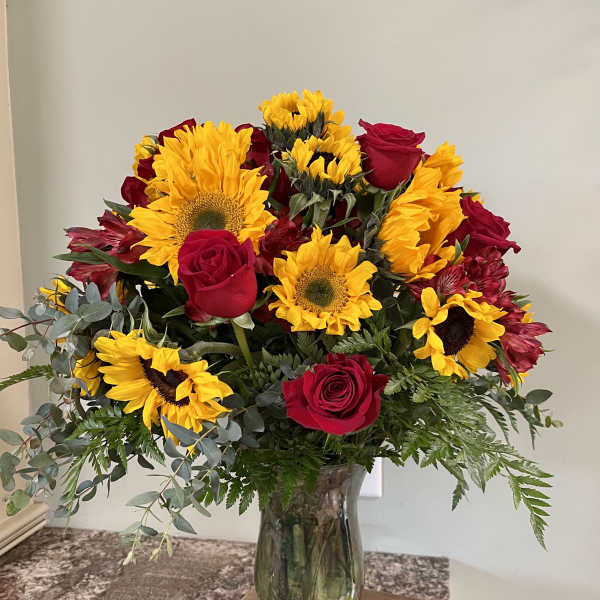 Bouquet of red roses and yellow sunflowers in a glass vase