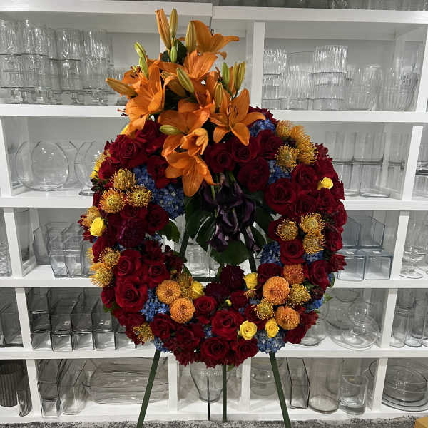 Large floral wreath on a stand with orange lilies and red roses