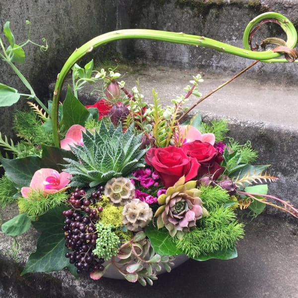 Mixed floral arrangement with red roses, succulents, and berries in a low container