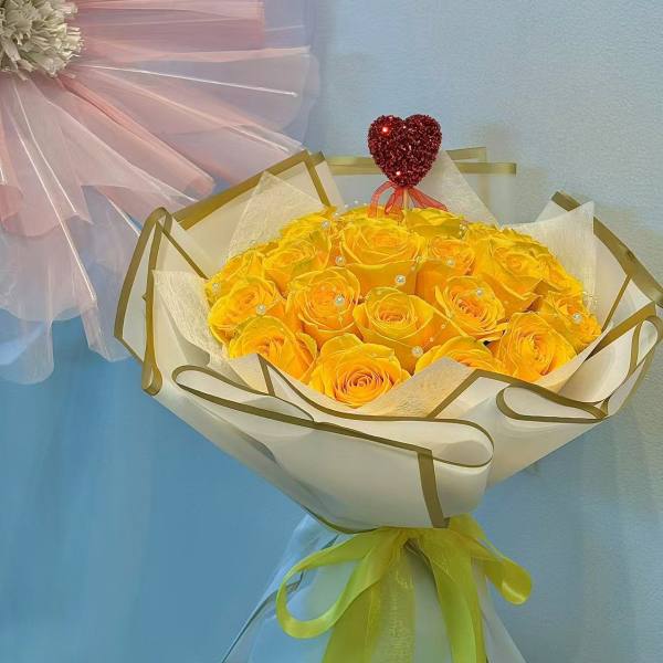 Bouquet of yellow roses wrapped in white paper with a red heart topper