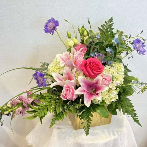 Pink roses and lilies arranged in a wooden container with purple accents
