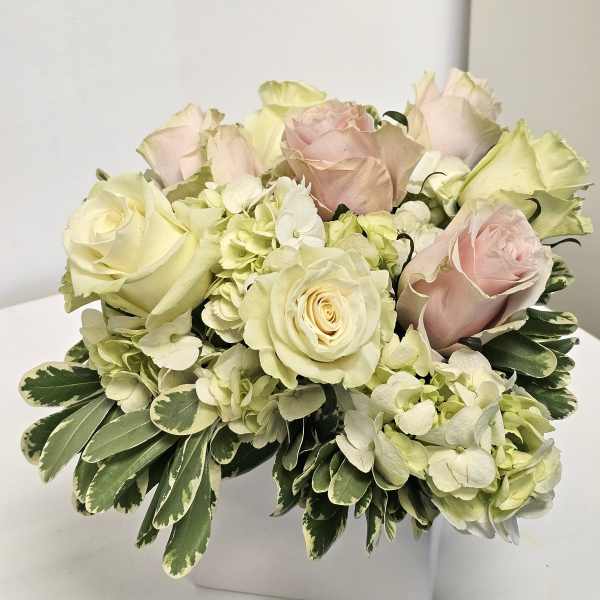 Arrangement of pale roses and hydrangeas in a white square vase