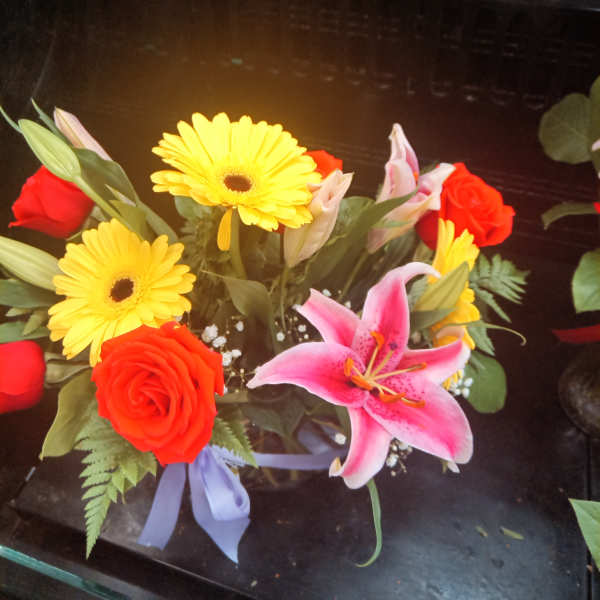 Bouquet with red roses, yellow gerbera daisies, and a pink lily in a vase