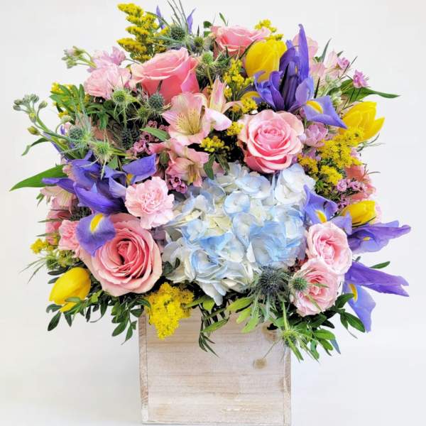 Mixed bouquet in a wooden box with pink roses, blue hydrangea, and purple irises