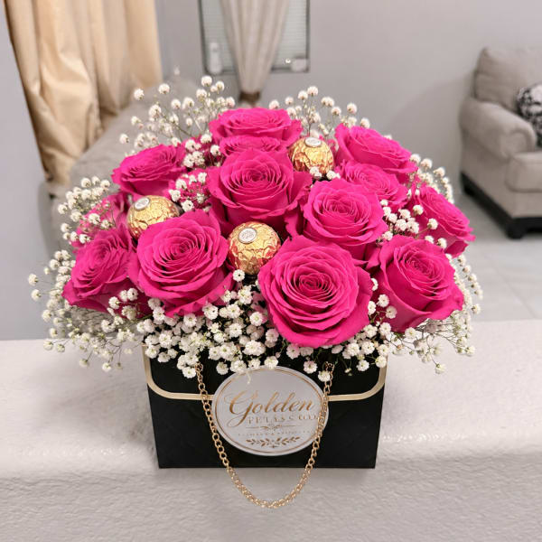 Hot pink roses in a black gift box with white filler flowers and gold chocolates