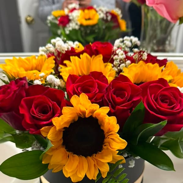 Red roses and yellow sunflowers arranged in a round black box with a ribbon