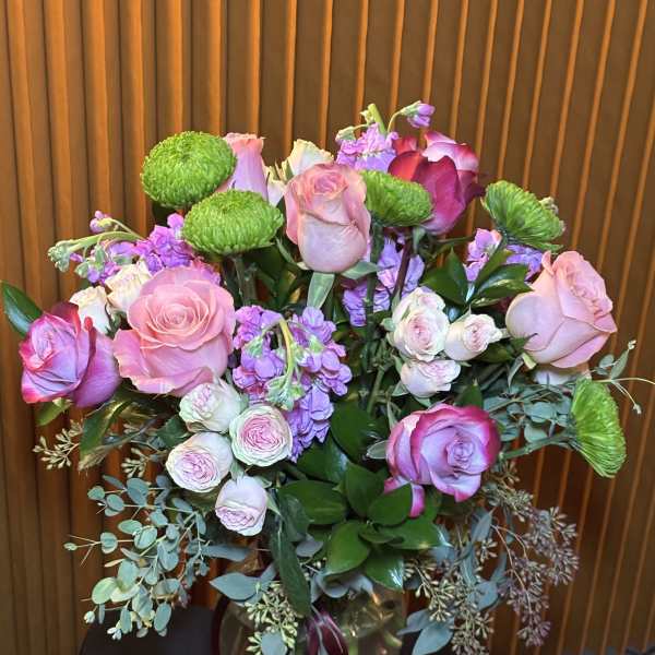 Pink and lavender roses in a glass vase with green button mums