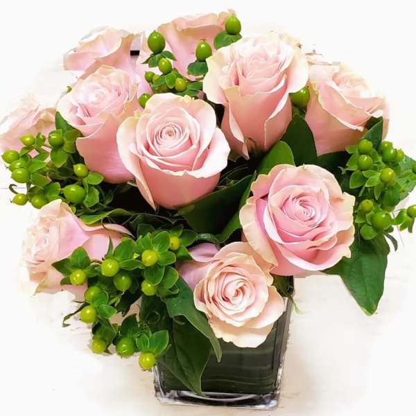 Pink roses arranged in a clear square vase with green berries