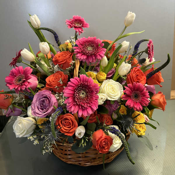 Mixed bouquet in a wicker basket with pink gerberas, roses, and white tulips