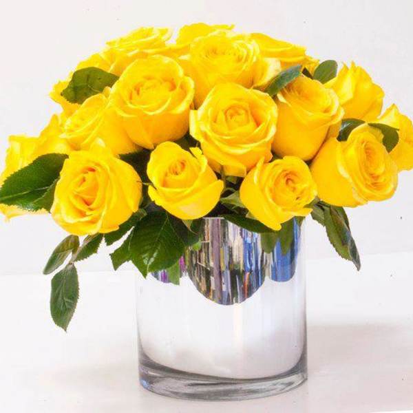Short glass vase filled with bright yellow roses in a compact arrangement