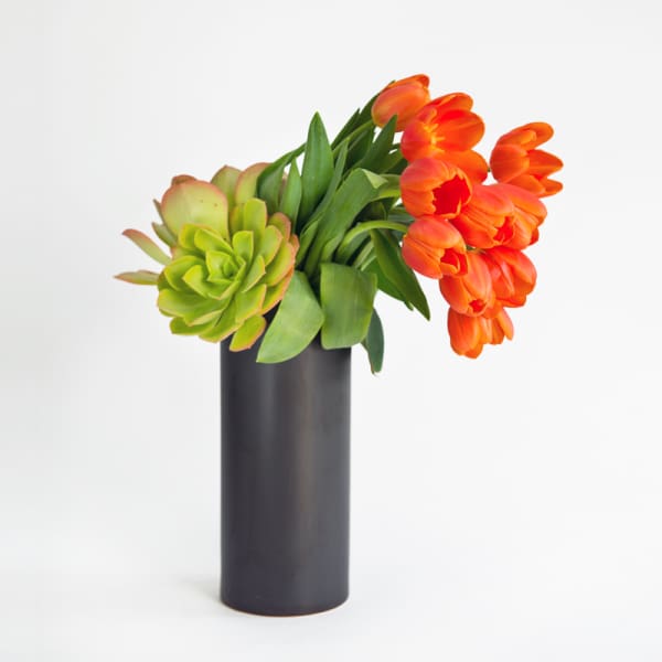 Orange tulips and a green succulent in a black vase