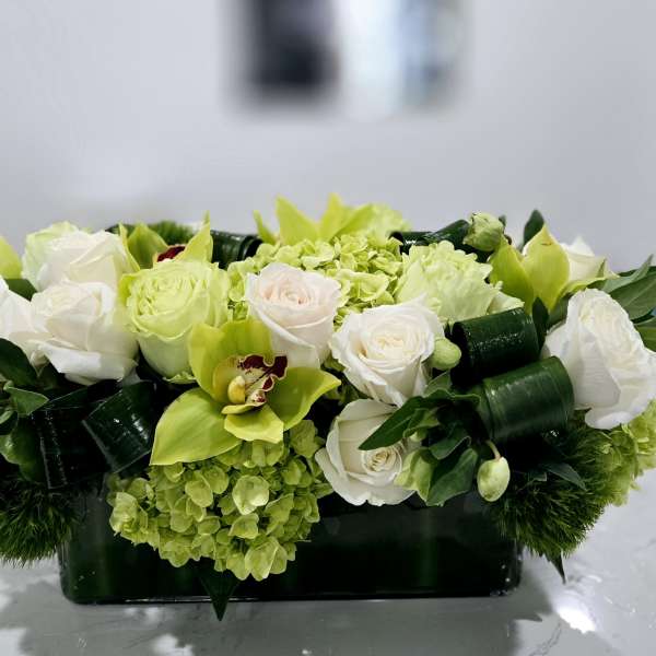 White roses and green orchids in a low rectangular vase