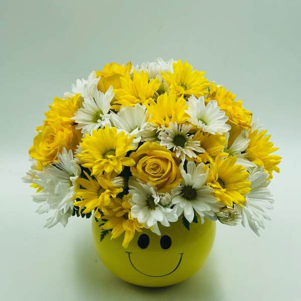 Yellow and white flowers arranged in a smiley-face pot