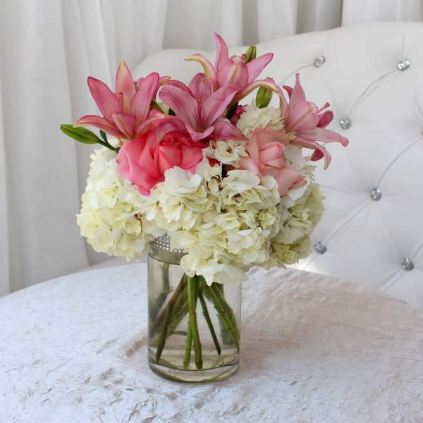 Pink lilies and roses arranged with white hydrangeas in a glass vase.
