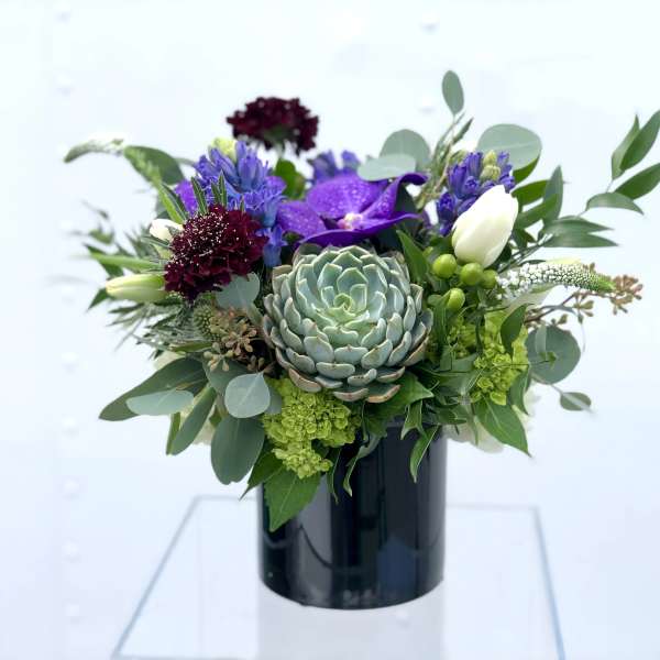 Purple and white floral arrangement with a succulent in a black vase