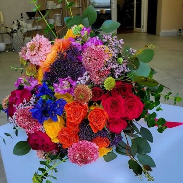 Colorful hand-tied bouquet of roses and mixed blooms in bright pink, orange, yellow, and purple tones