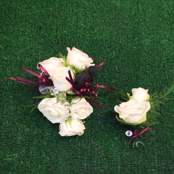 White rose boutonnieres with burgundy ribbon on green turf