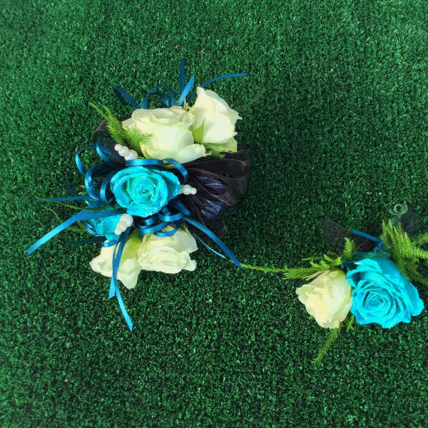 Two small rose corsages with blue ribbon accents on green turf