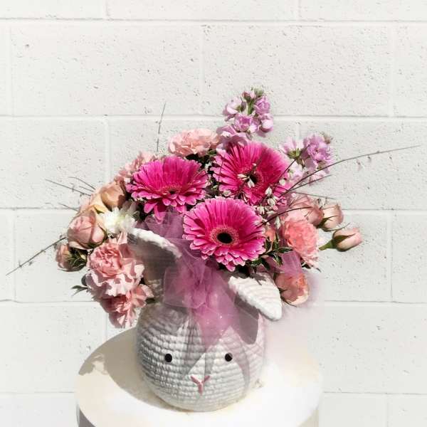 Pink floral arrangement in a textured bunny-shaped container with a tulle bow