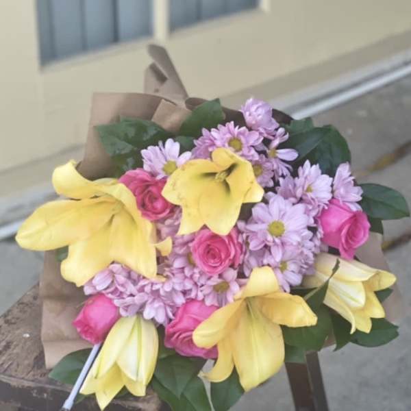 Bouquet of yellow lilies, pink roses, and lavender daisies wrapped in brown paper