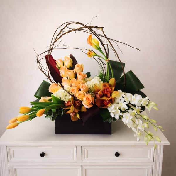 Arrangement of peach roses, white orchids, and orange calla lilies in a black box
