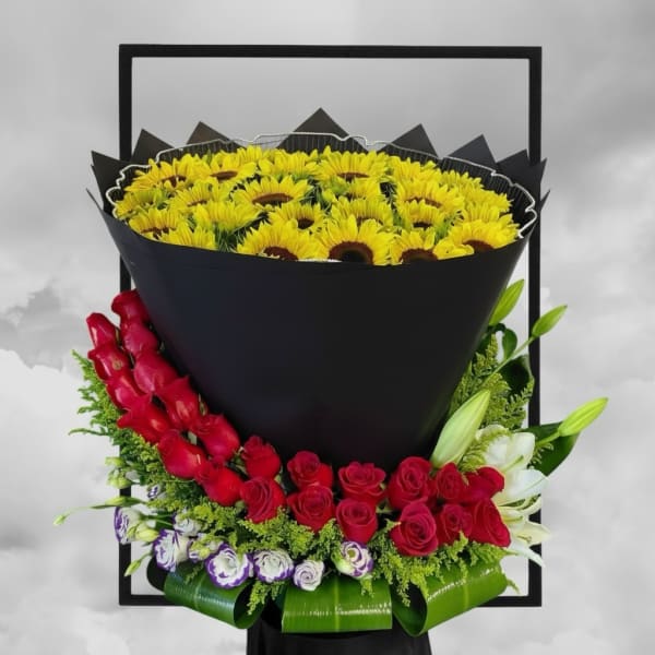 Large bouquet of yellow sunflowers with red roses and white lilies in black wrap