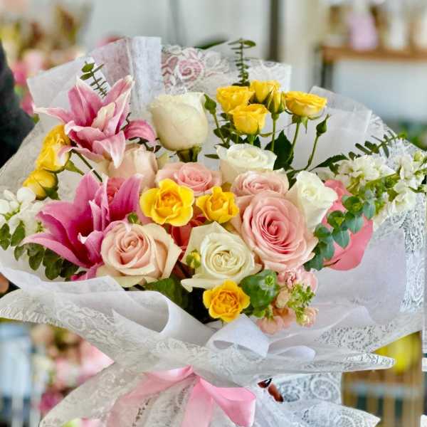 Bouquet of pink, white, and yellow roses with lilies wrapped in lace paper