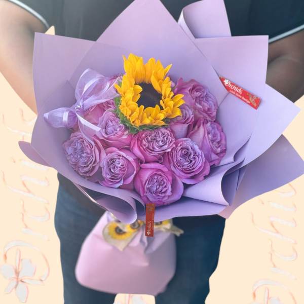 Bouquet of purple roses with a yellow sunflower center wrapped in lavender paper