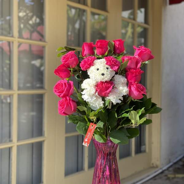 Pink roses arranged around a small white teddy bear in a pink vase