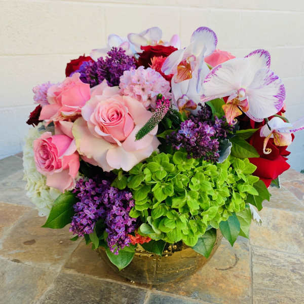 Pink roses and white orchids in a gold vase with purple blooms