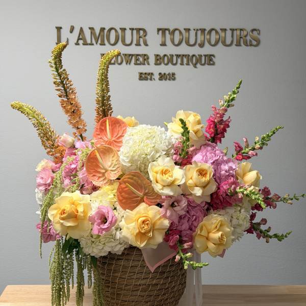Basket arrangement of pink, yellow, and white flowers with orange anthuriums