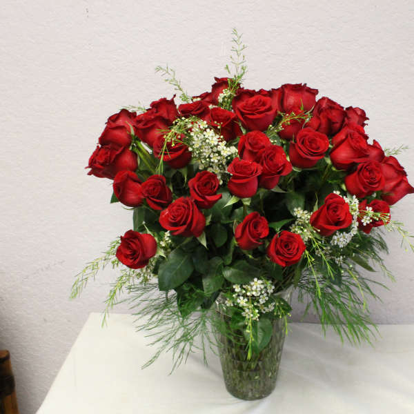 Red roses arranged in a clear glass vase with small white filler flowers